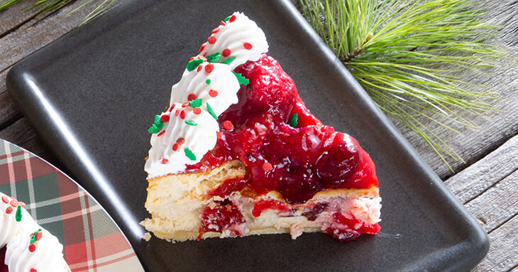 Indulge in our Holiday cheesecake featuring a delicious cookie crust, slow-baked with creamy Wisconsin cream cheese, layered with tart cranberry and cherry filling, and topped with silky buttercream for the perfect festive dessert!