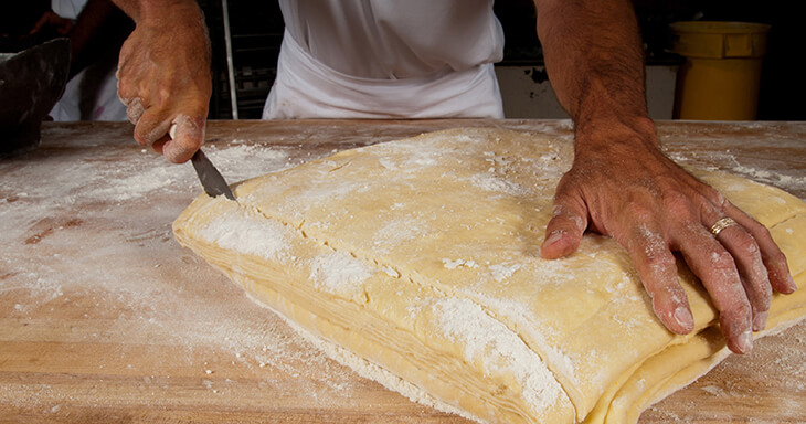 A skilled baker cuts dough at O&H Danish Bakery, showcasing our commitment to scratch-made pastries and uncompromising quality.