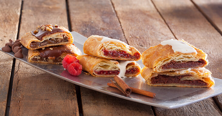 Slices of Raspberry Kringle with ruby red raspberries, buttery Cinnamon Roll Kringle, and rich Turtle Kringle, showcasing a delightful trio of tart, sweet, and decadent flavors.