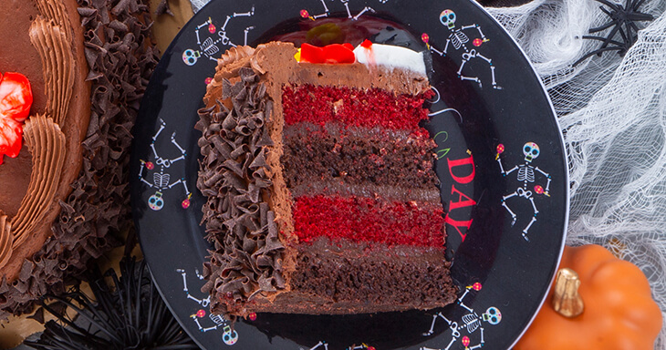 A beautifully decorated red velvet and chocolate cake with layers made from buttermilk and Dutch cocoa, topped with dark chocolate silk filling and adorned with a festive calavera, perfect for Halloween or the Day of the Dead.