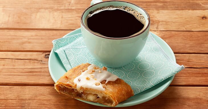 Slice of Harvest Kringle with a cup of coffee.