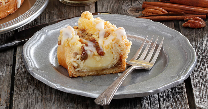 A delicious coffee cake featuring flaky pastry layered with silky smooth custard over rich butterscotch filling, topped with buttery streusel and pecans, perfect for pairing with a warm cup of coffee.