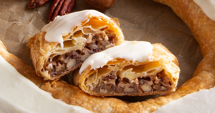 An oval-shaped Danish Kringle filled with a rich pecan filling and drizzled with sweet icing is a Racine Kringle pastry.