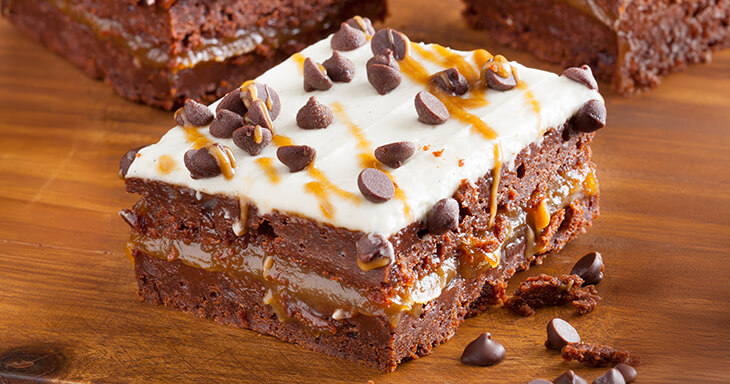 Vanilla Bean frosted triple layer fudge brownies drizzles with caramel and chocolate chips.